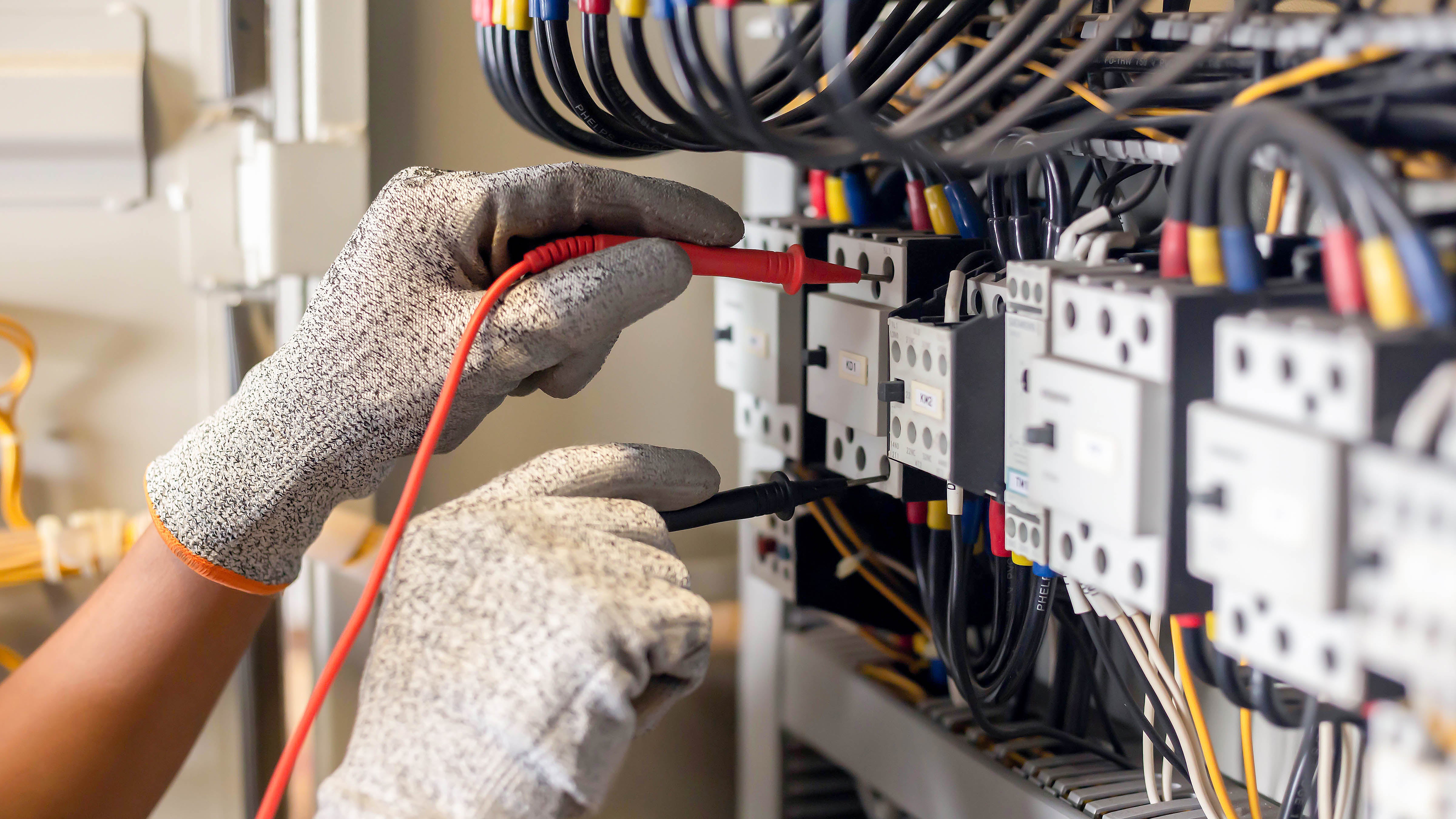 Engineer testing current with a multimeter in a system control cabinet