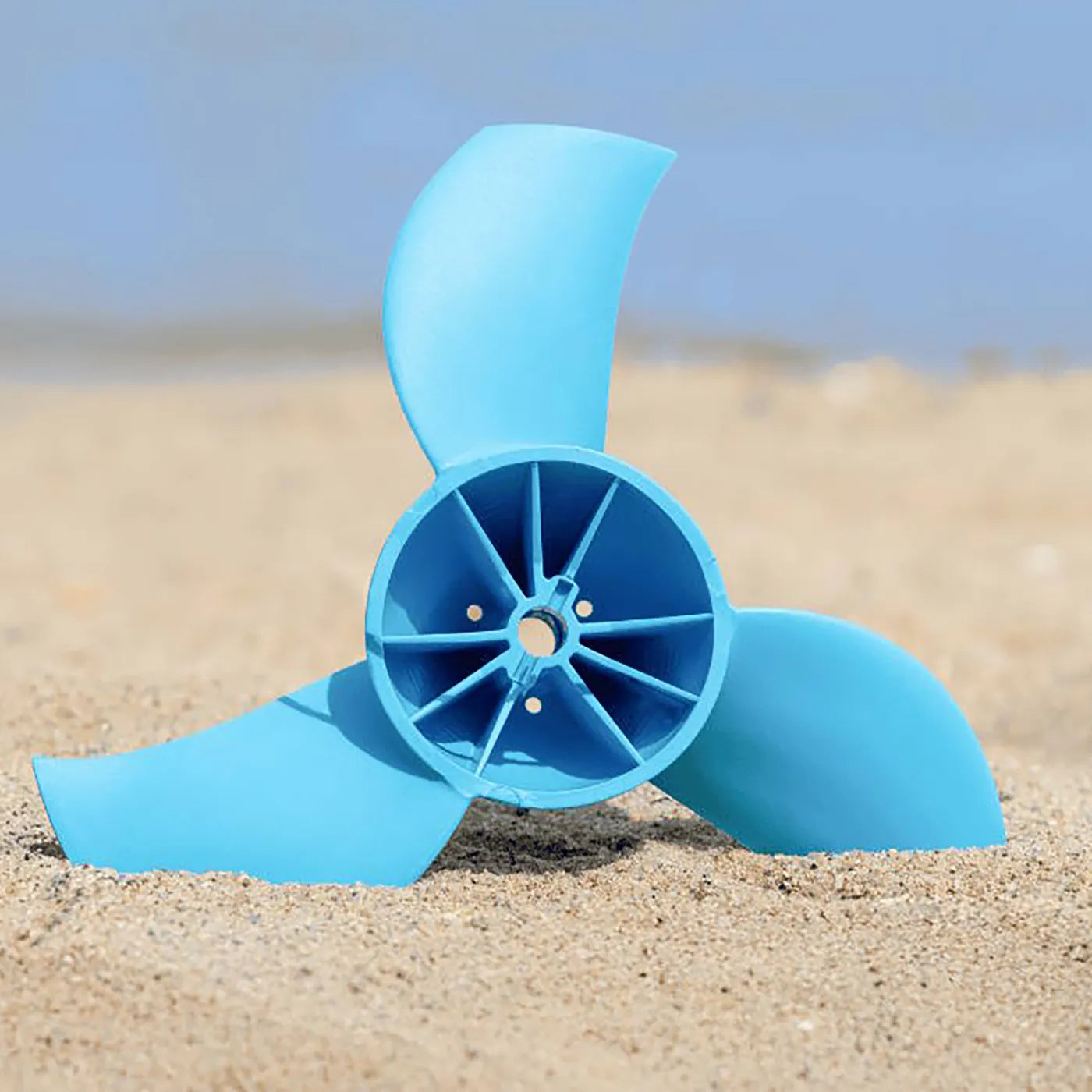 Blue propeller-like object on a sandy surface with a blurred blue sky background